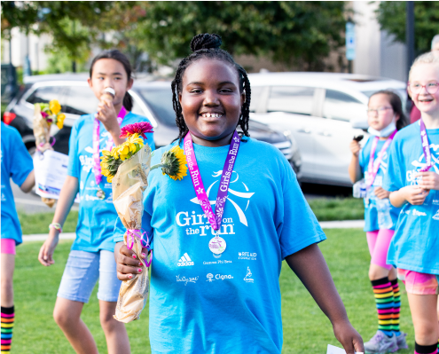 A Girls on the Run participant smiles while holding a bouquet of yellow flowers 